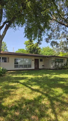 Single-story residence featuring a broad front lawn, mature trees, and a prominent front window