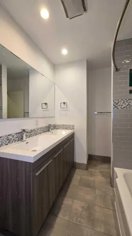 Dual vanity with integrated sinks, wood-finish cabinetry, mosaic tile backsplash, and large format floor tiling