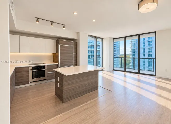 Kitchen featuring wood-finish cabinetry, white solid-surface countertops, stainless steel appliances, wood-finish flooring, and floor-to-ceiling glass panel windows