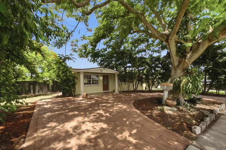 Paver driveway with a curved design, mature trees, and a landscaped garden bed