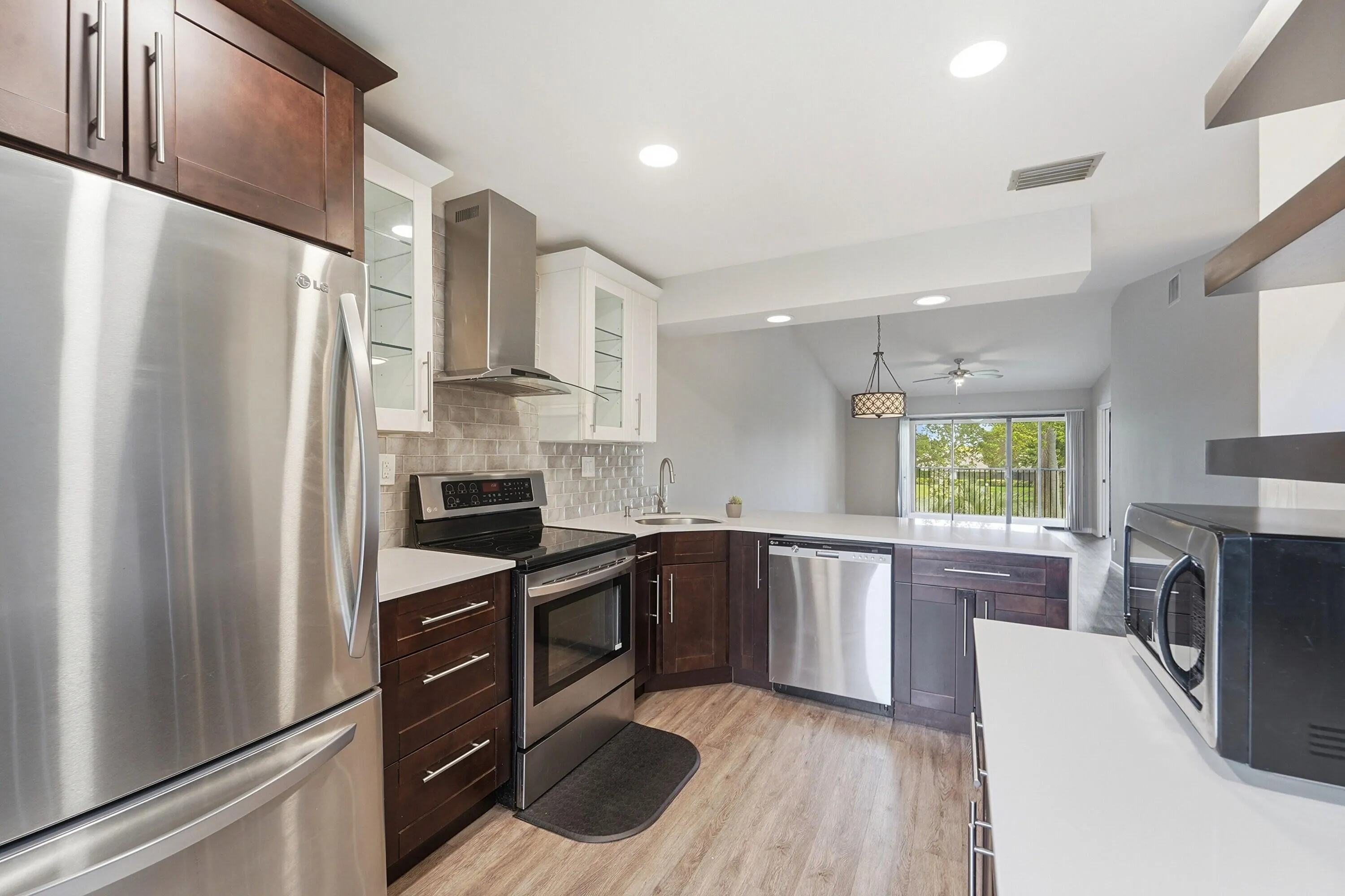 Modern kitchen featuring stainless steel appliances, dark wood cabinetry with brushed metal hardware, subway tile backsplash, and wood-finish flooring