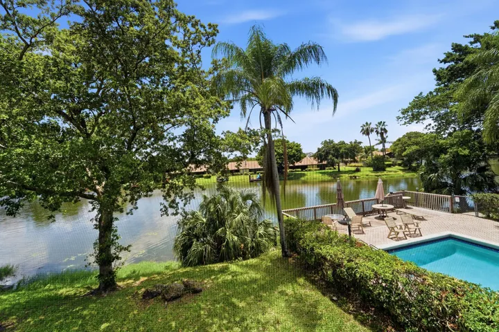 Waterfront property featuring a private swimming pool, spacious deck with wood railing, lush green landscaping, and mature trees
