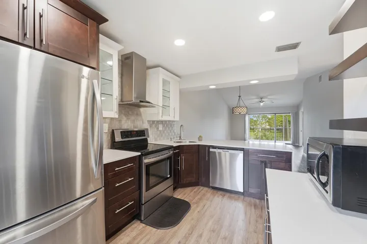 Modern kitchen featuring stainless steel appliances, dark wood cabinetry with brushed metal hardware, subway tile backsplash, and wood-finish flooring
