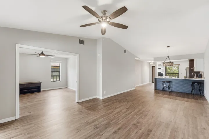 Wood-finish flooring throughout, light gray wall color, two ceiling fans with integrated lighting, kitchen island with seating, and stainless steel appliances