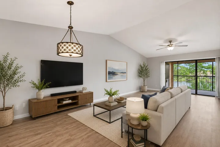 Vaulted ceiling living area featuring wood-finish flooring, a contemporary chandelier, and sliding glass doors opening to a screened balcony overlooking a body of water