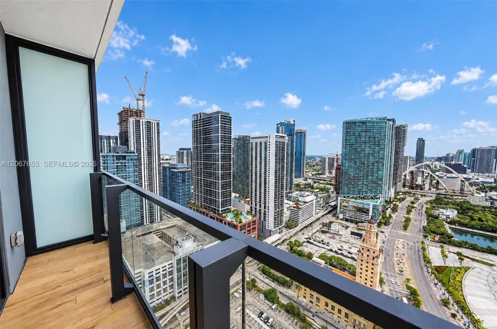 Private balcony featuring wood-finish decking, glass panel railing, and metal framing with a panoramic urban skyline backdrop