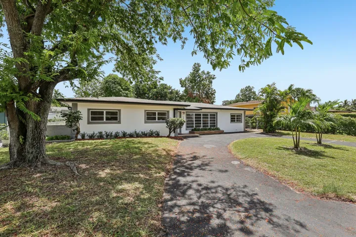Front exterior view showing the home's entry, driveway, mature trees, and landscaped yard.