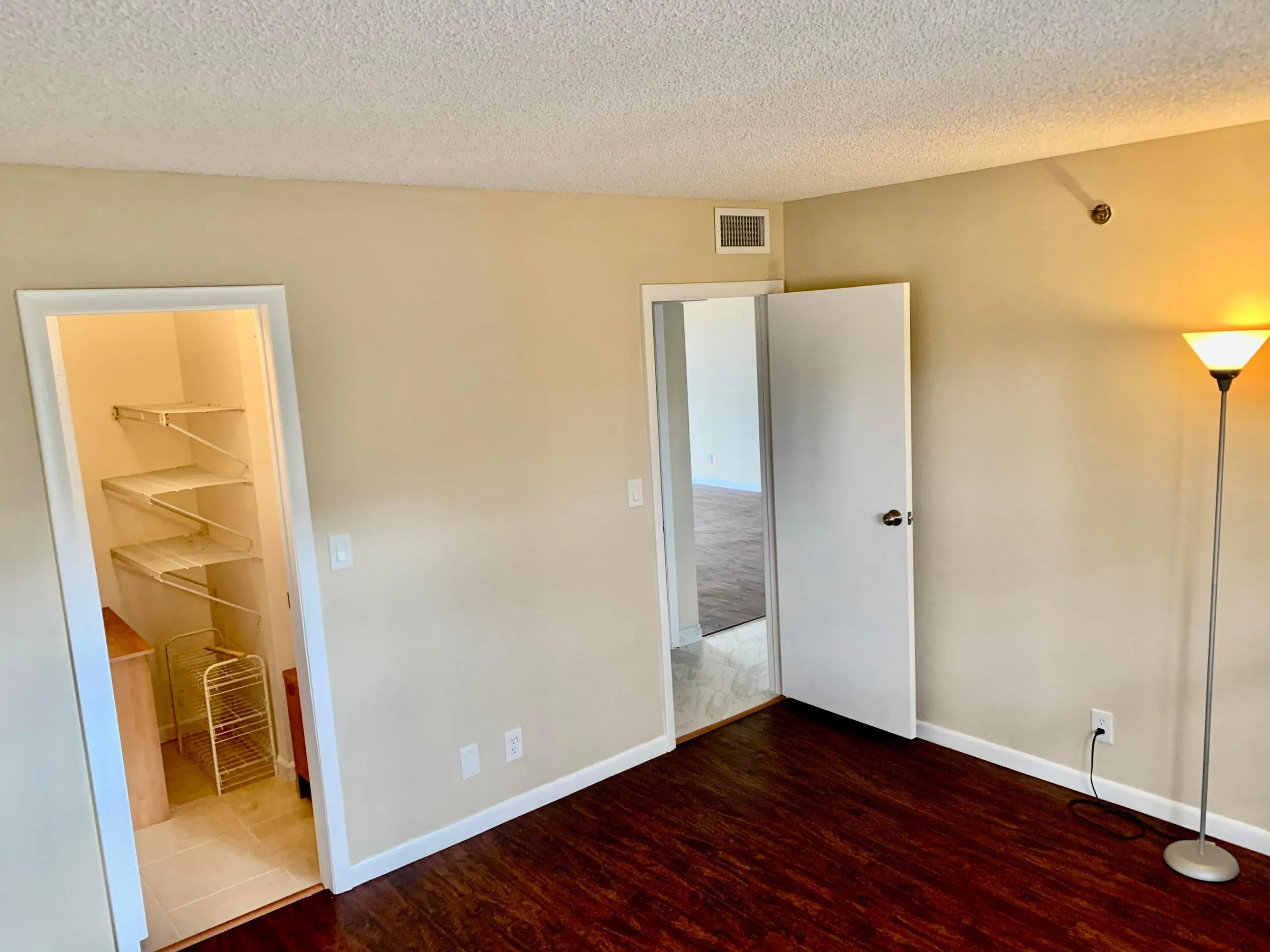 Spacious room featuring dark wood-finish flooring, light neutral-toned walls, and white baseboards