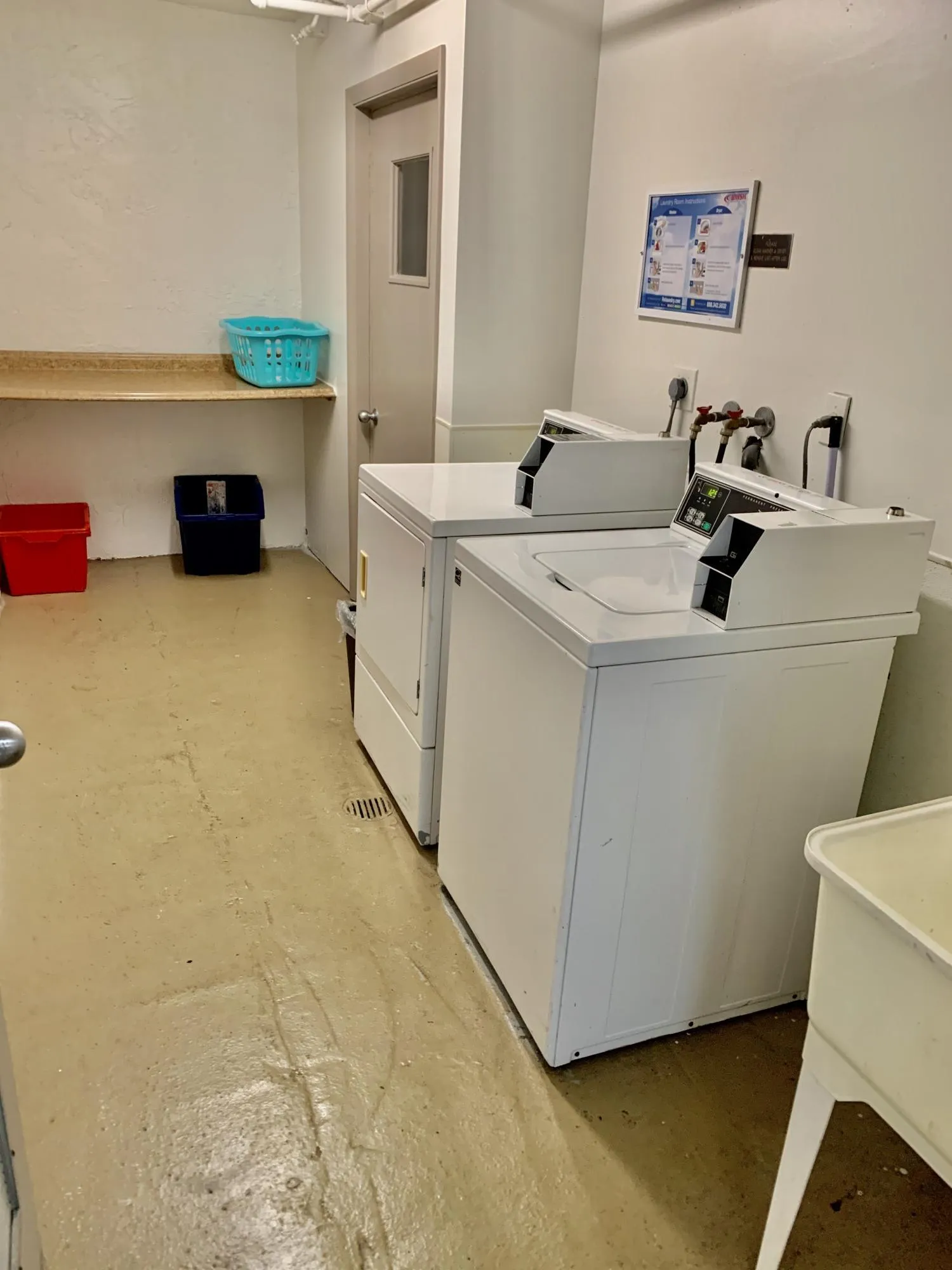 Dedicated laundry area featuring white top-load washing machines, a utility sink, and a wall-mounted shelving unit