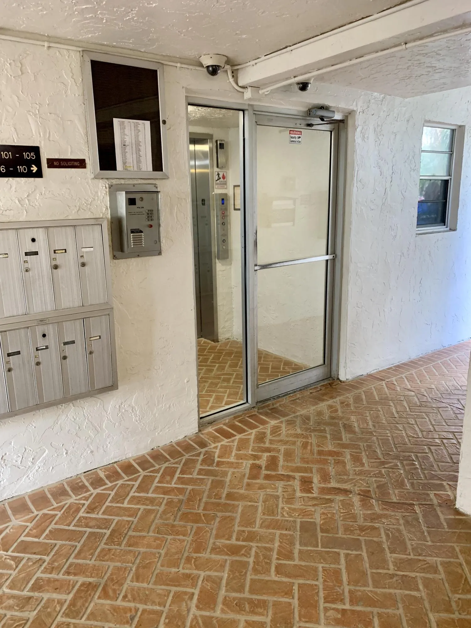 Entryway featuring a herringbone brick floor pattern, white stucco walls, and a glass-paneled entry door