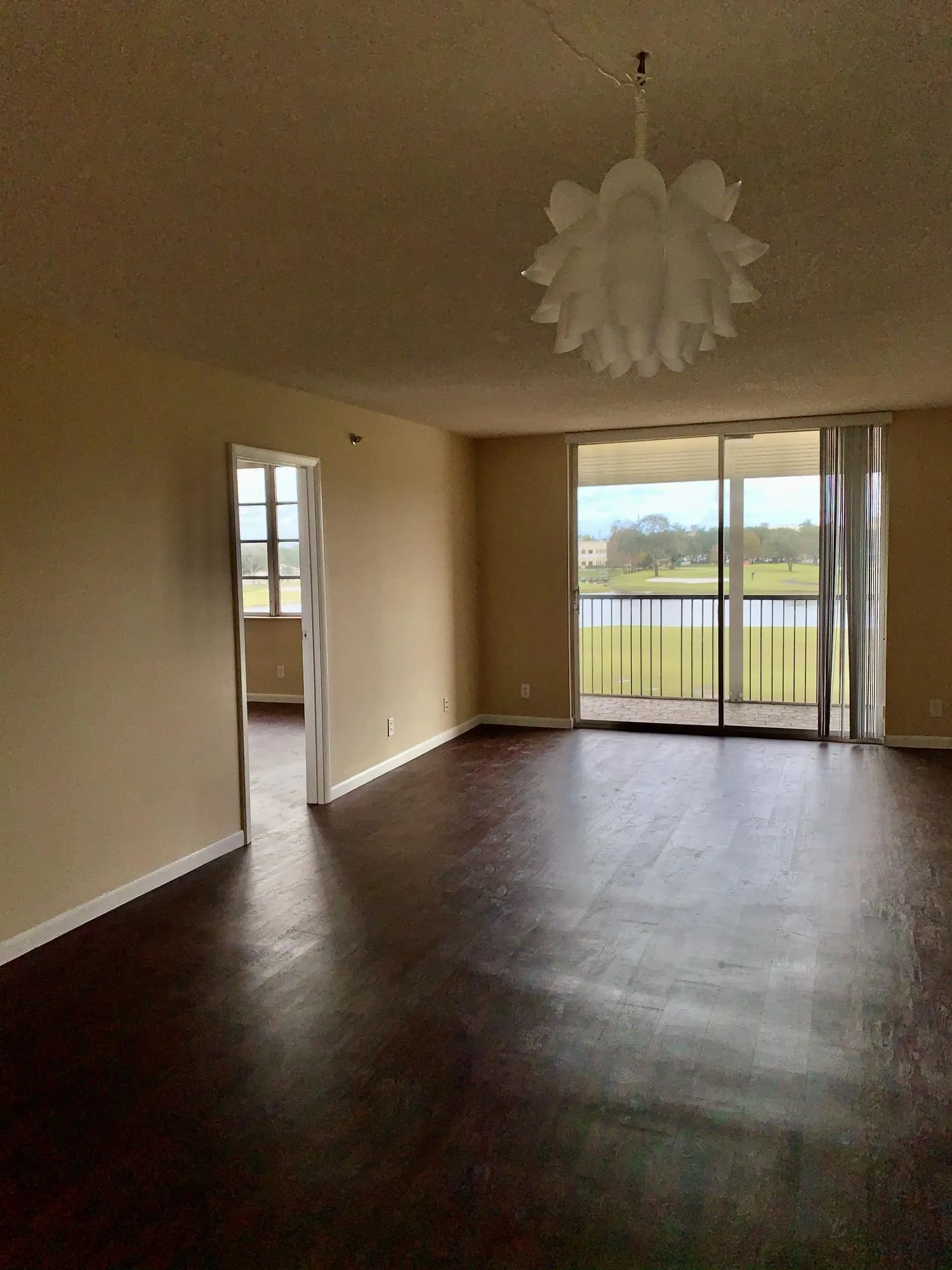 Spacious room featuring dark wood-finish flooring, neutral wall tones, and a distinctive chandelier