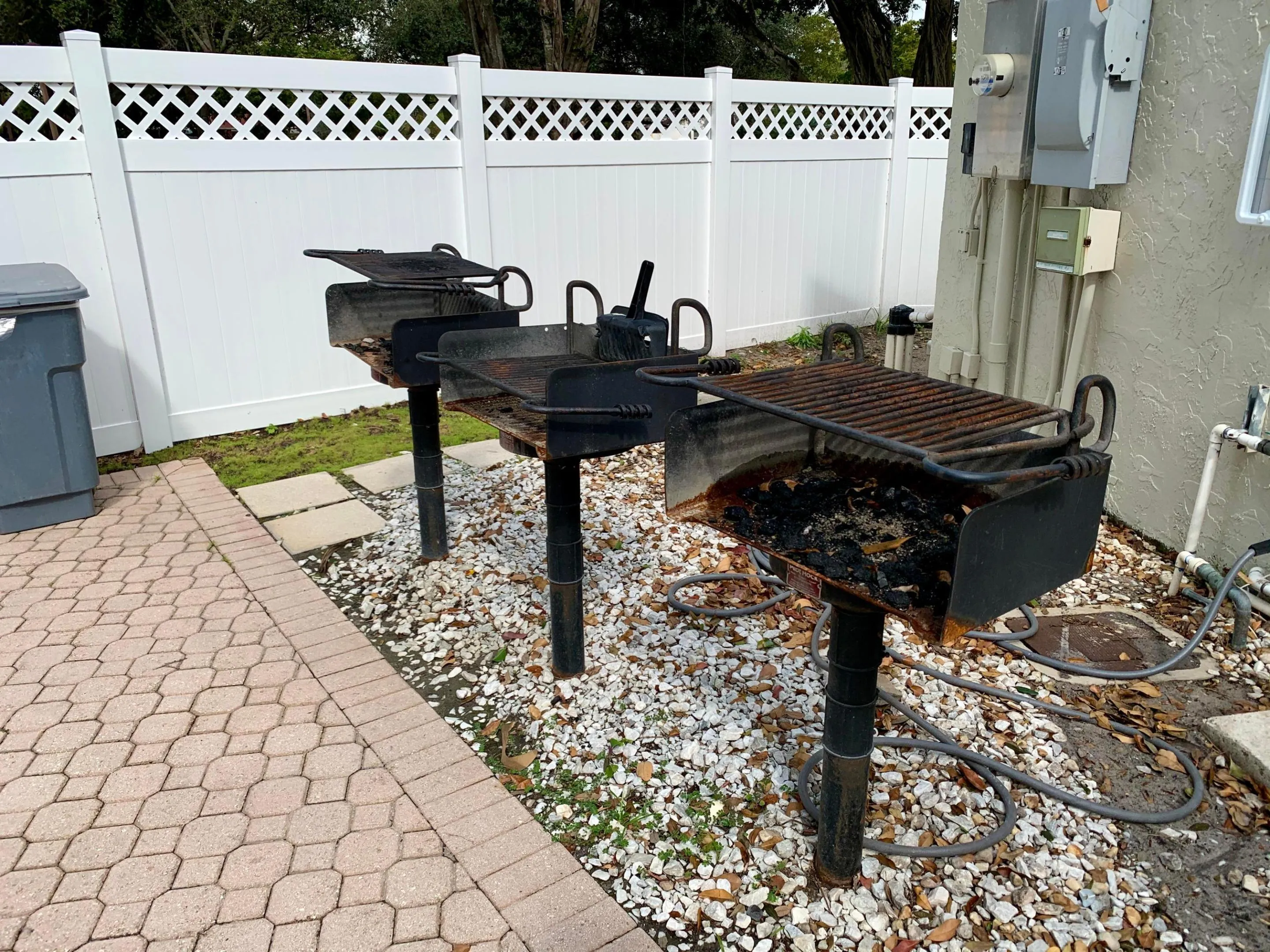 Paved patio area featuring multiple built-in charcoal grills on a gravel base