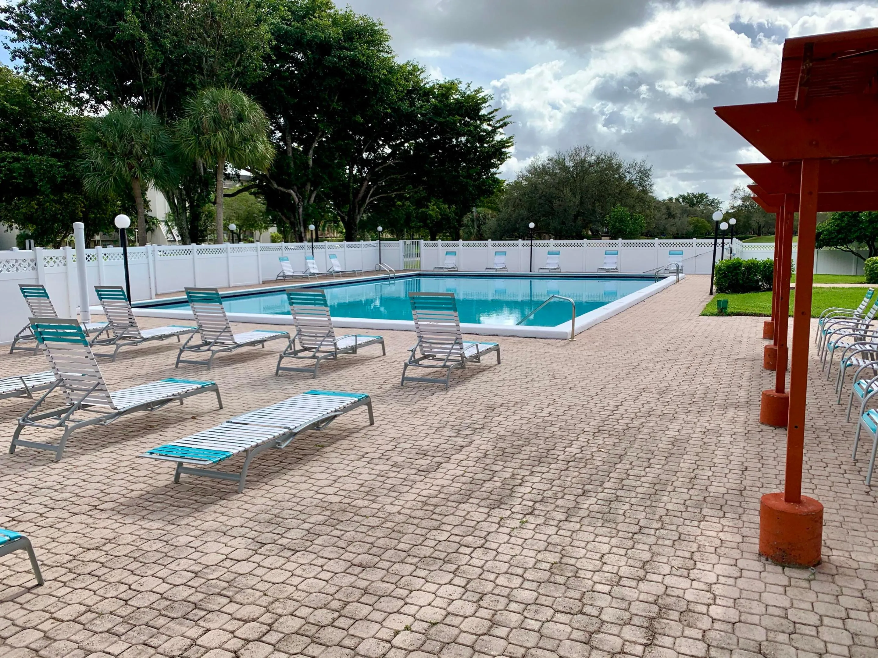 Community swimming pool featuring a perimeter fence, surrounding paver decking, and an adjacent pergola structure