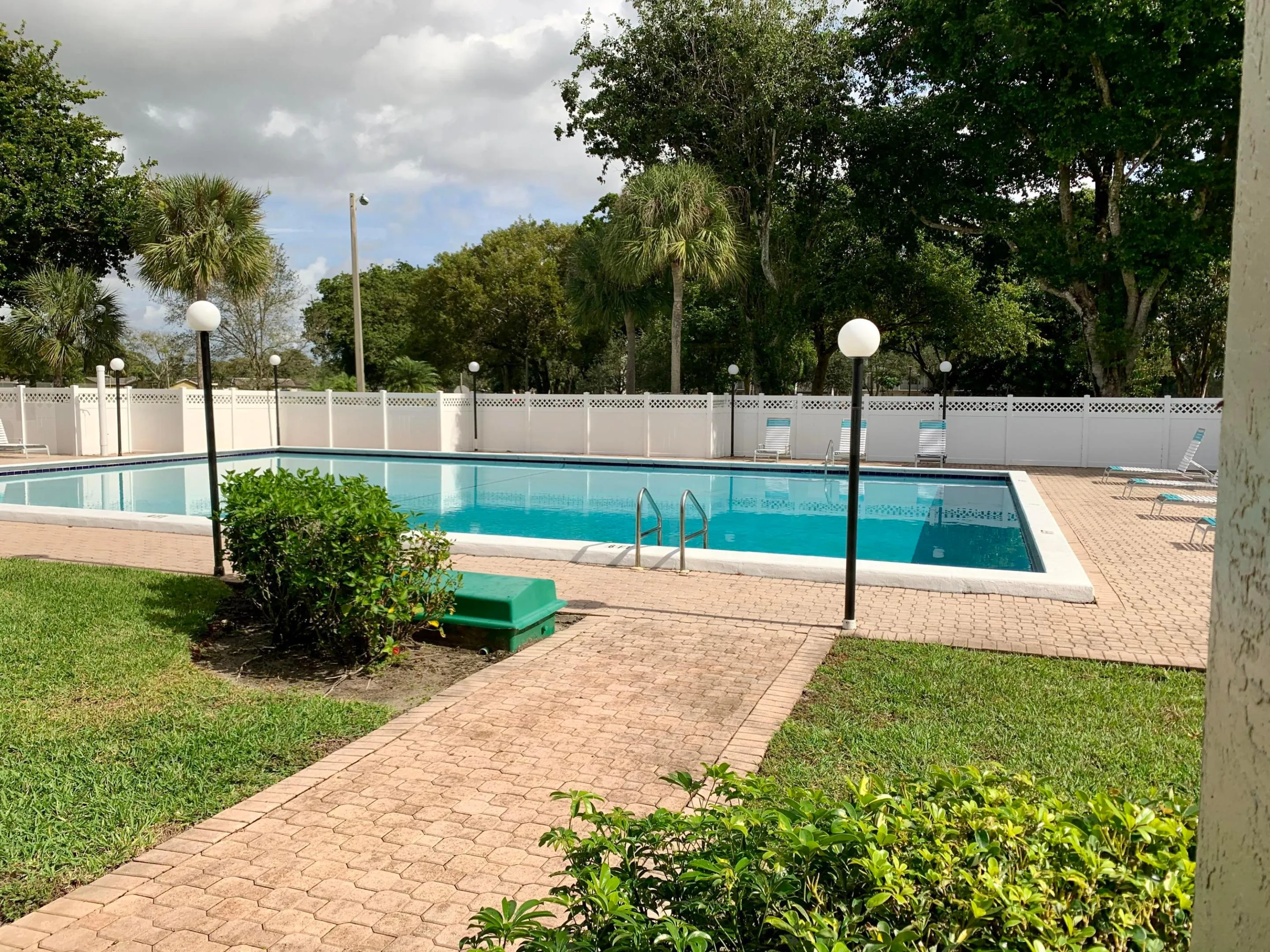 Swimming pool with white perimeter fencing, surrounding paver decking, and integrated lighting
