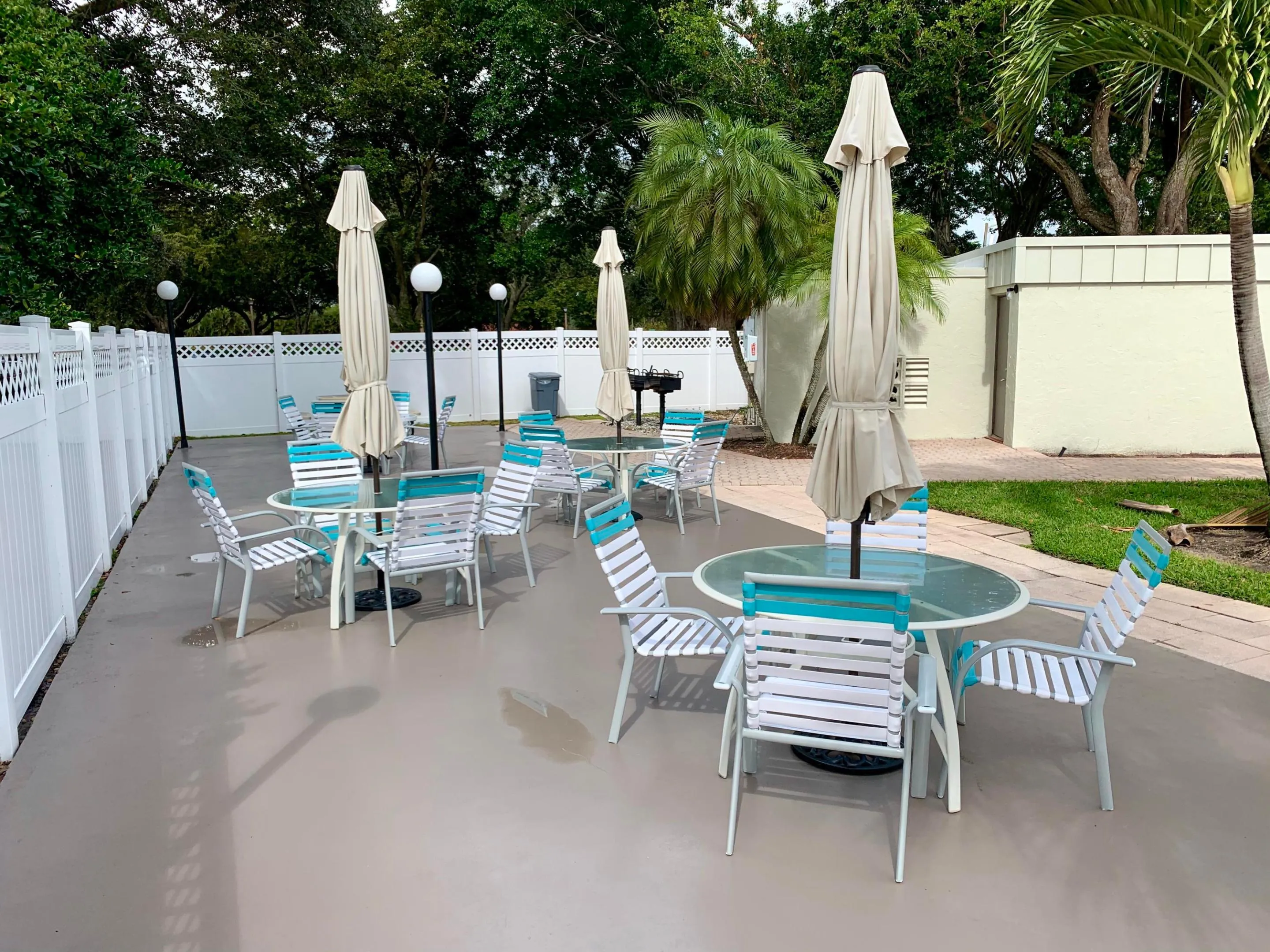 Spacious outdoor patio area featuring multiple seating arrangements, a built-in barbecue grill, perimeter fencing, and mature landscaping