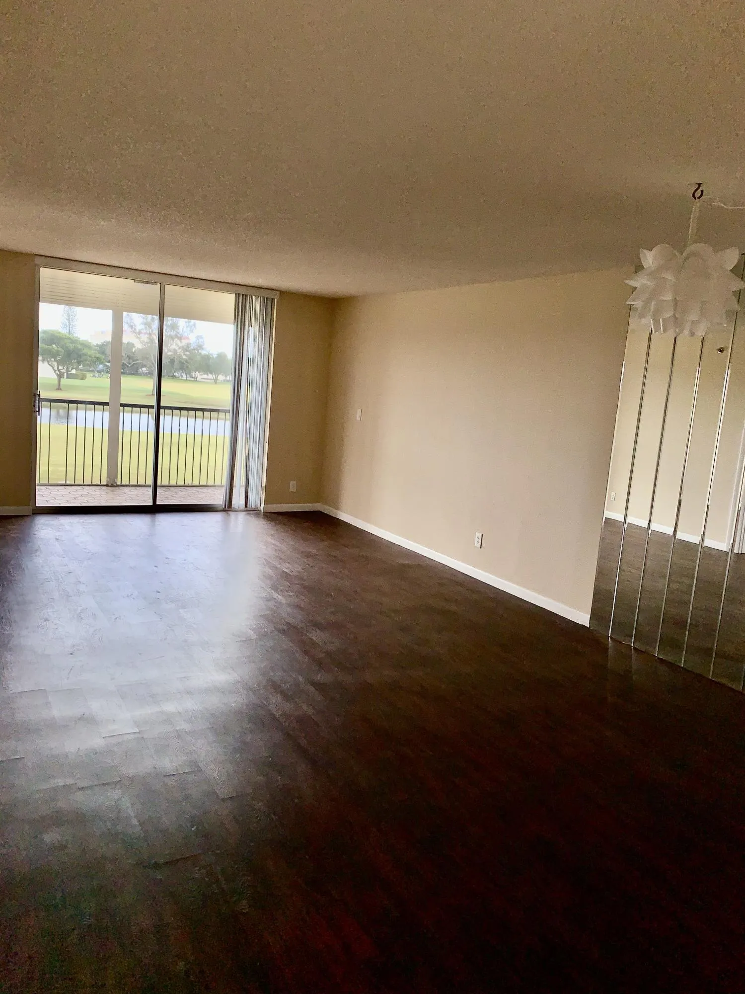 Spacious interior featuring dark wood-finish flooring, neutral wall tones, and a sliding glass door leading to a private balcony
