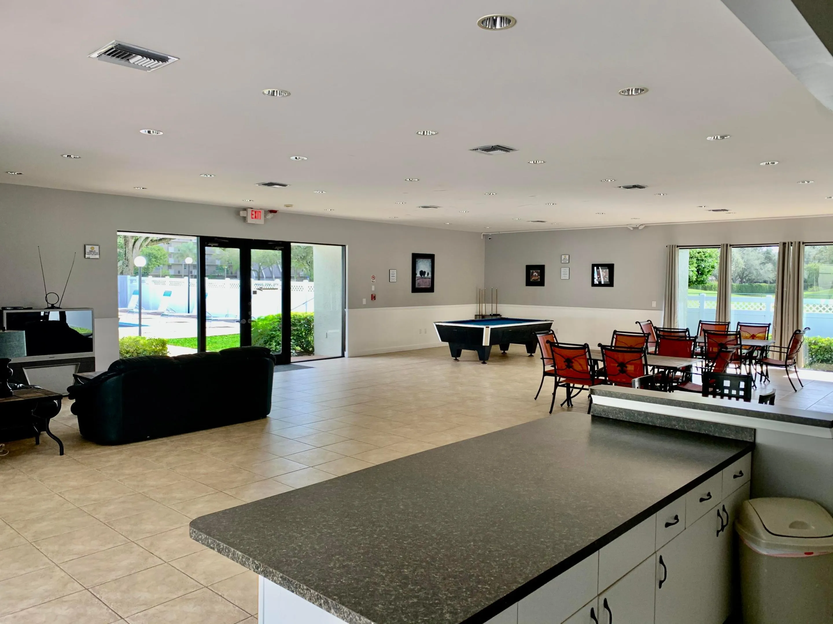 Expansive common area featuring tiled flooring, recessed lighting, a built-in counter with cabinetry, and large glass doors providing natural light