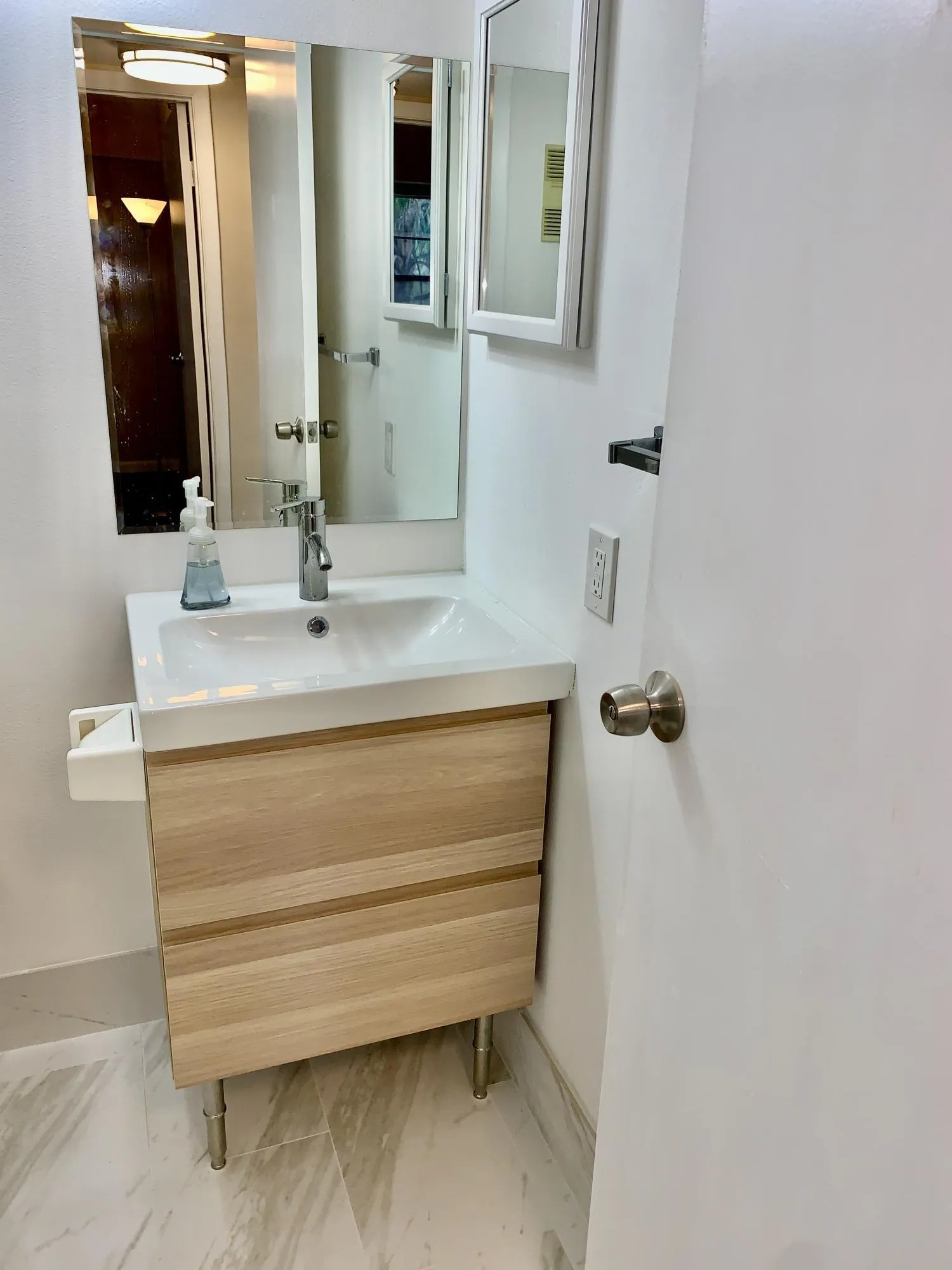 Modern vanity featuring a white integrated sink, chrome faucet, and light wood-finish cabinetry on metal legs