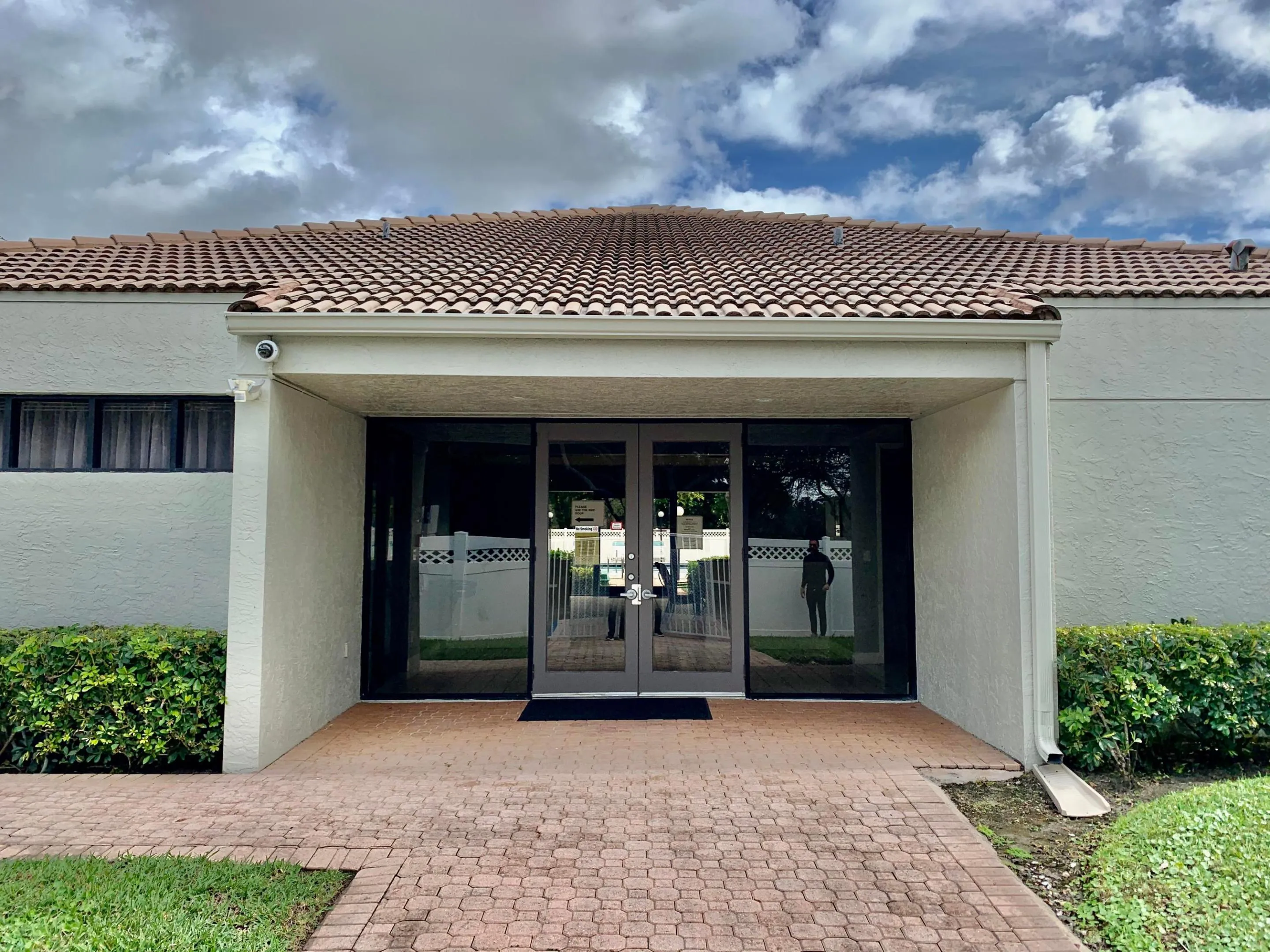Entryway featuring a terra cotta tile roof, large glass double doors, a brick paver pathway, and surrounding landscaping