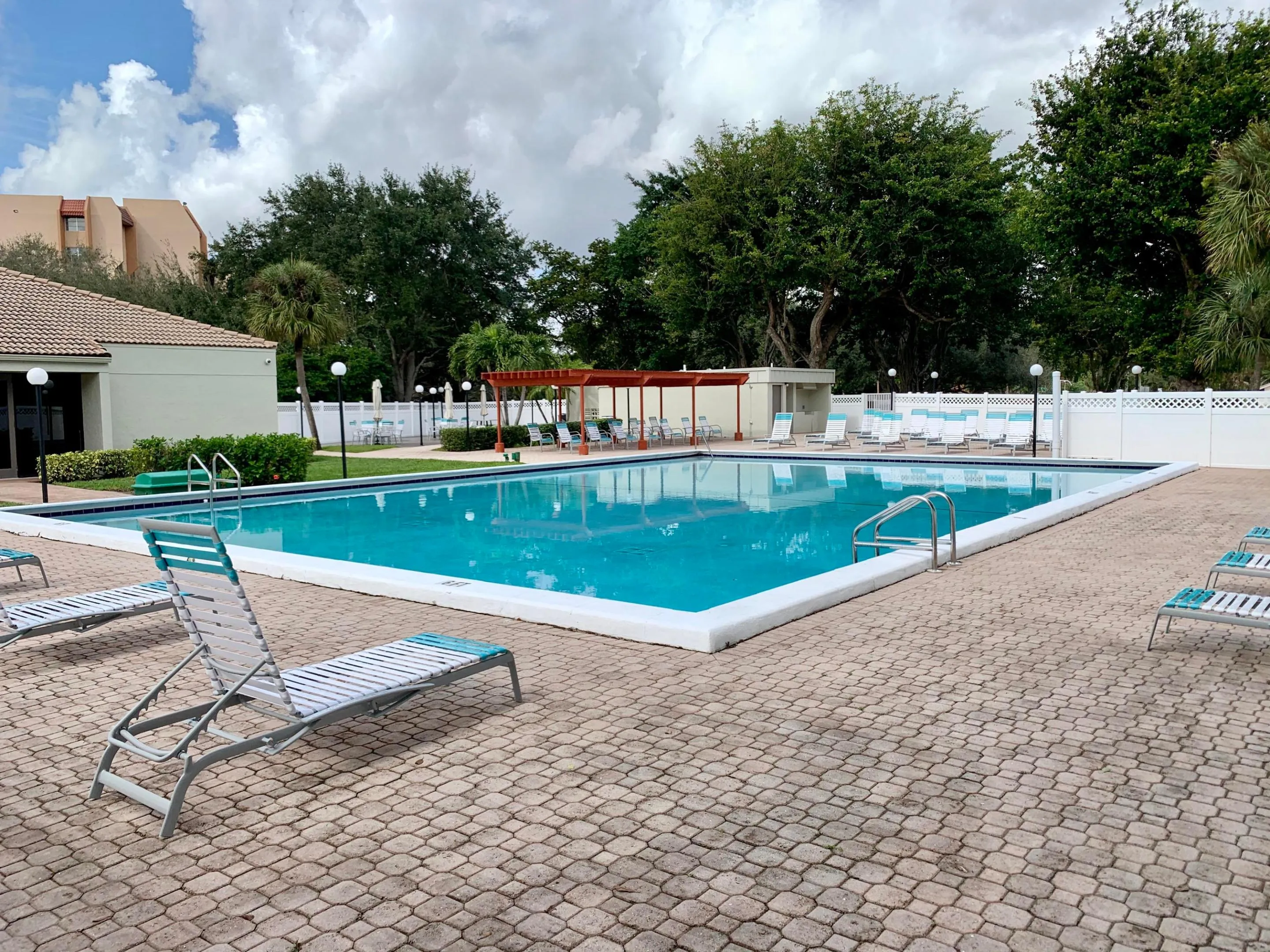 Spacious outdoor pool area featuring a rectangular pool with integrated steps, surrounding paver decking, and a white lattice fence