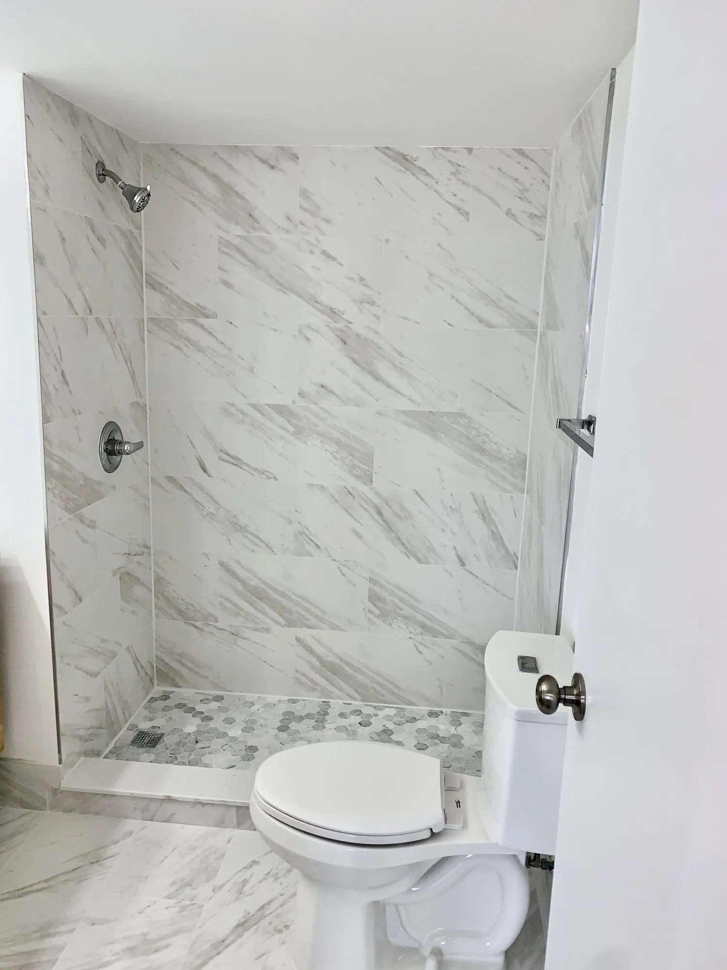 Bathroom featuring a walk-in shower with large format marble-look tile walls, a hexagonal mosaic tile shower pan, and a toilet