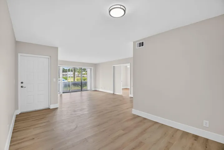 Spacious room featuring wood-finish flooring, a white entry door, and a sliding glass door to an outdoor area