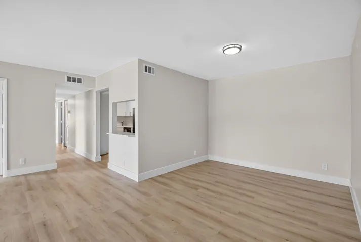 Spacious room featuring wood-finish flooring, light neutral wall paint, and a pass-through window with a breakfast bar