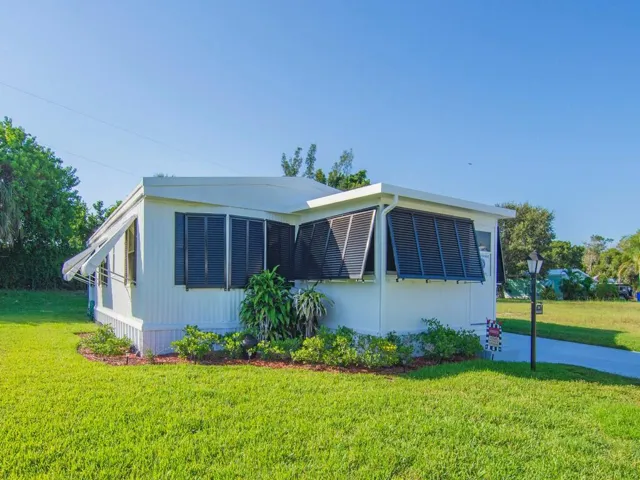 White horizontal siding, black louvered shutters, green manicured lawn, and lush landscaping