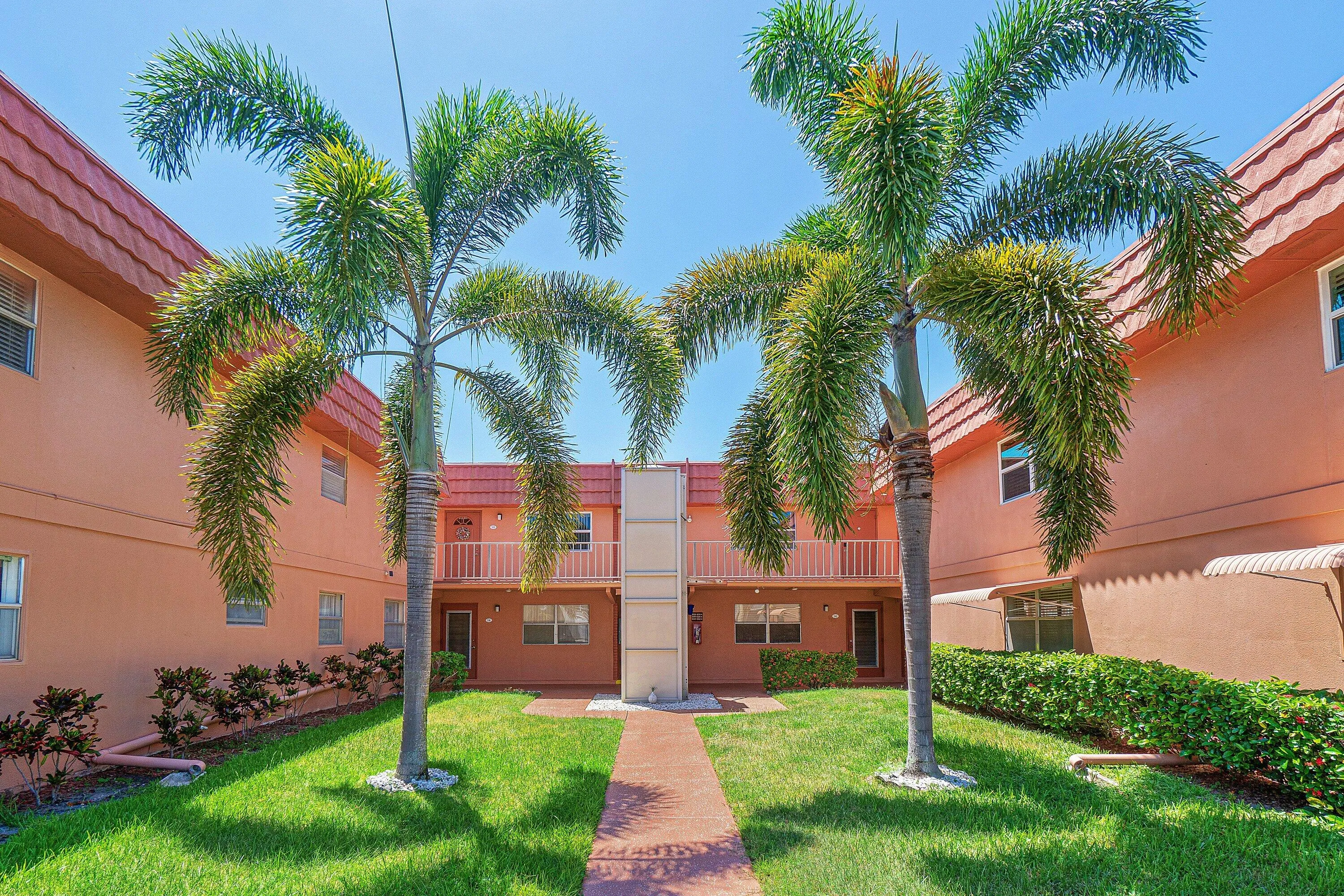 Manicured lawn, mature palm trees, tiled roof, second-story balcony, and paved walkway