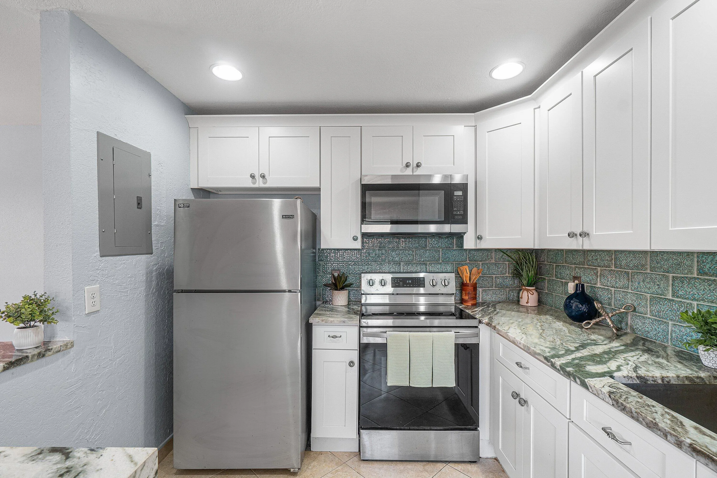 White shaker cabinetry, stainless steel appliances, patterned backsplash, recessed lighting, and patterned countertops