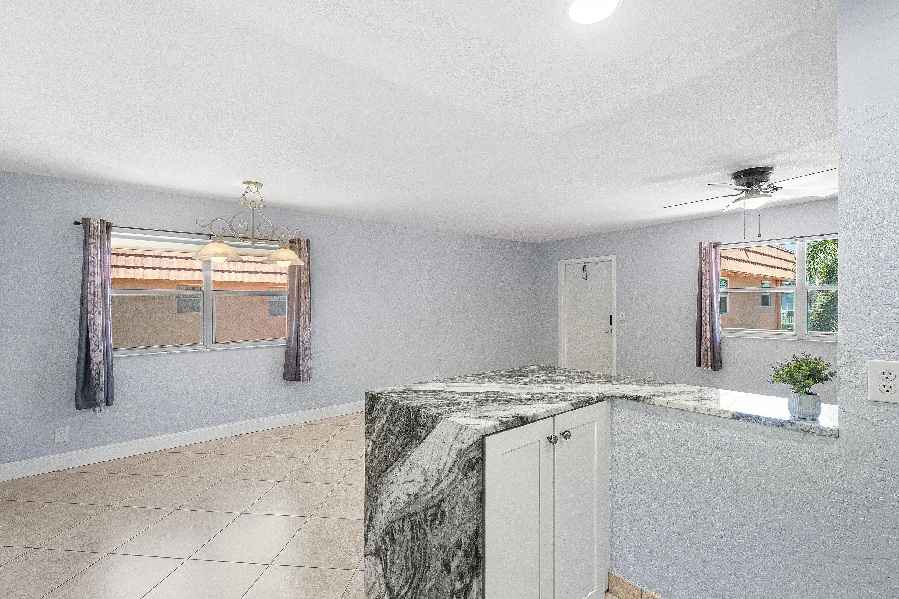 Open-concept room featuring a stone-finish waterfall island, tile flooring, and multiple windows