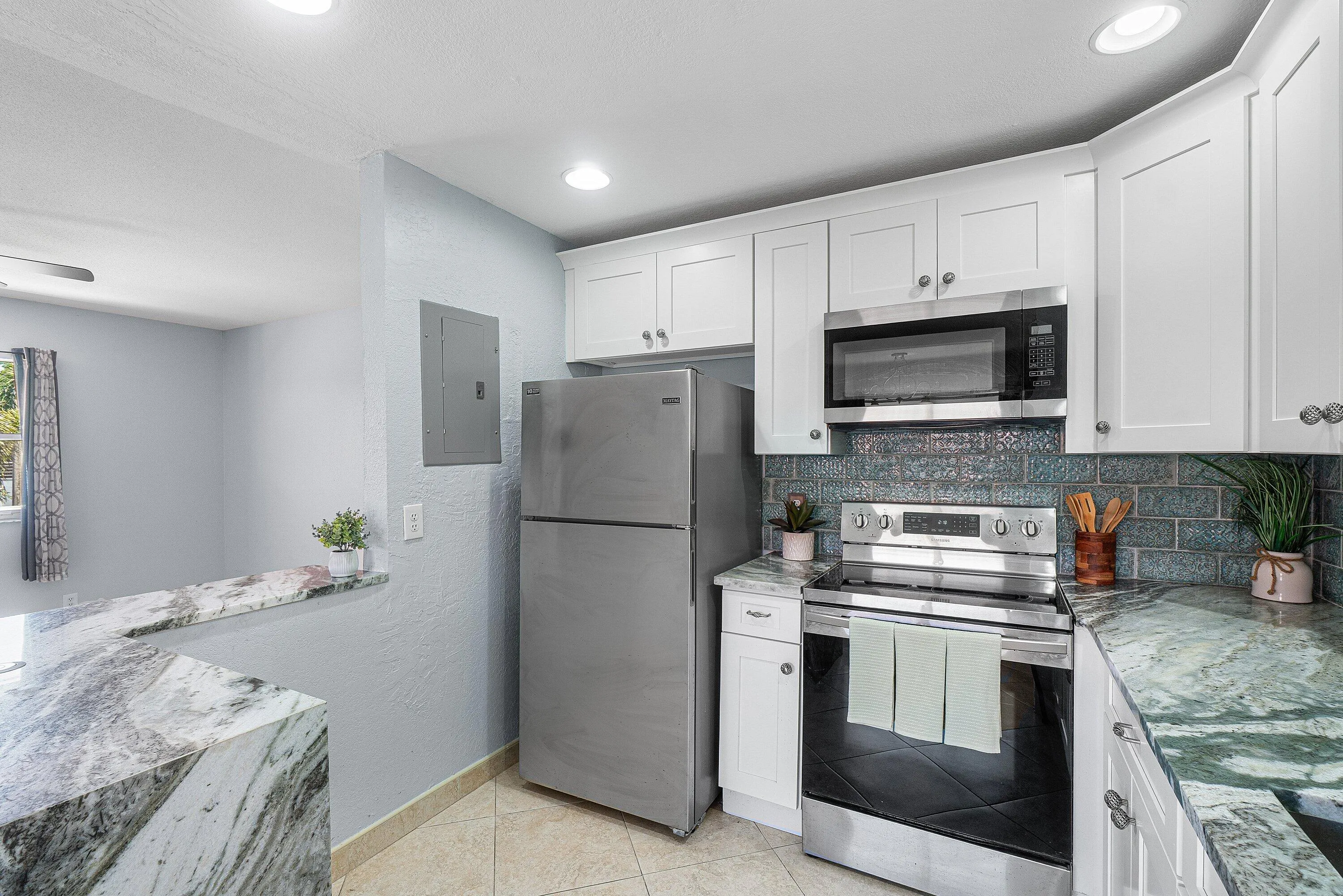 White shaker-style cabinetry with stainless steel hardware, stainless steel appliances, vibrant blue subway tile backsplash, recessed lighting, and multi-toned stone countertops