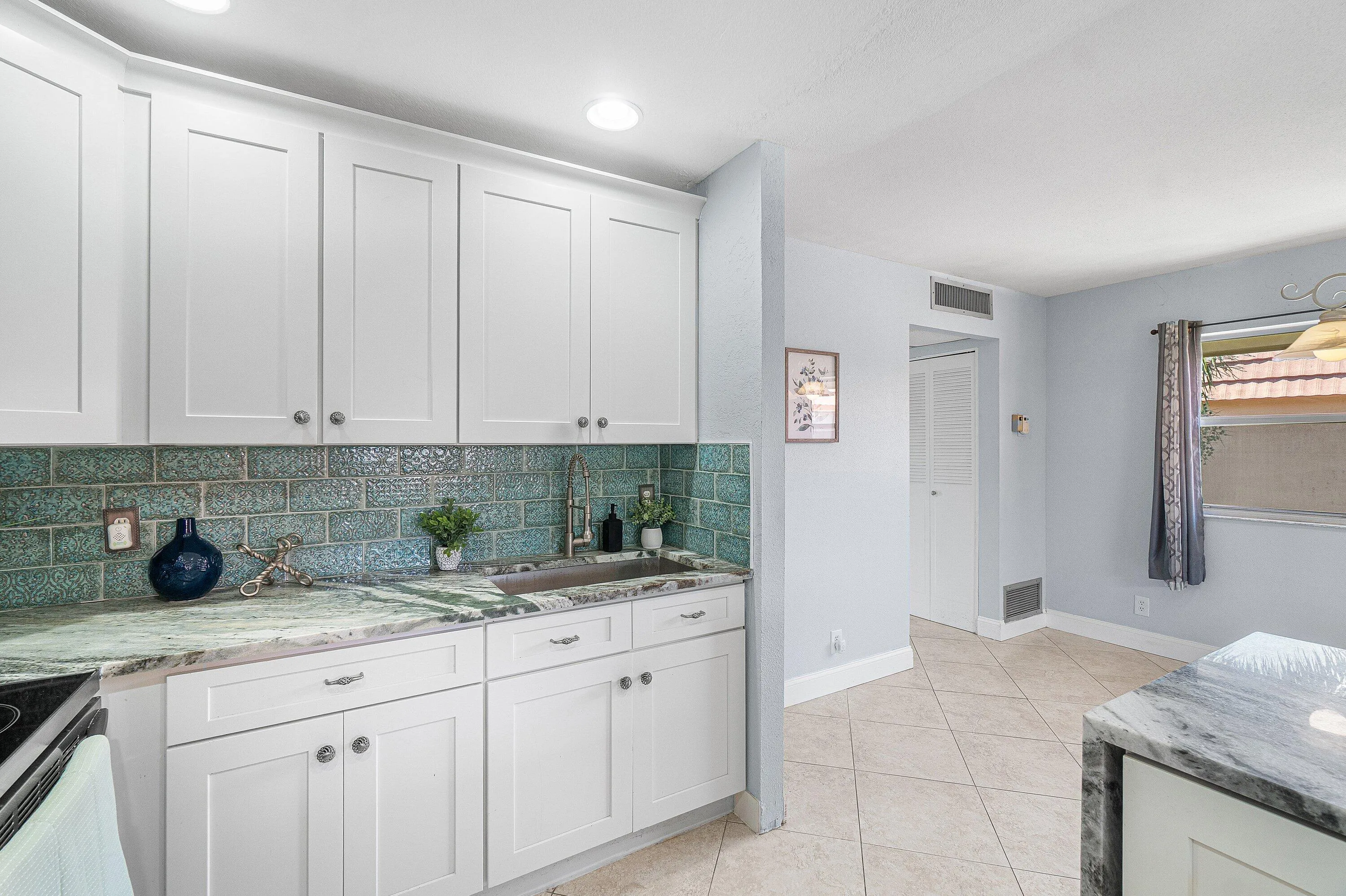 White shaker-style cabinetry, patterned tile backsplash, integrated sink with a gooseneck faucet, light-toned tiled flooring, and recessed ceiling lighting
