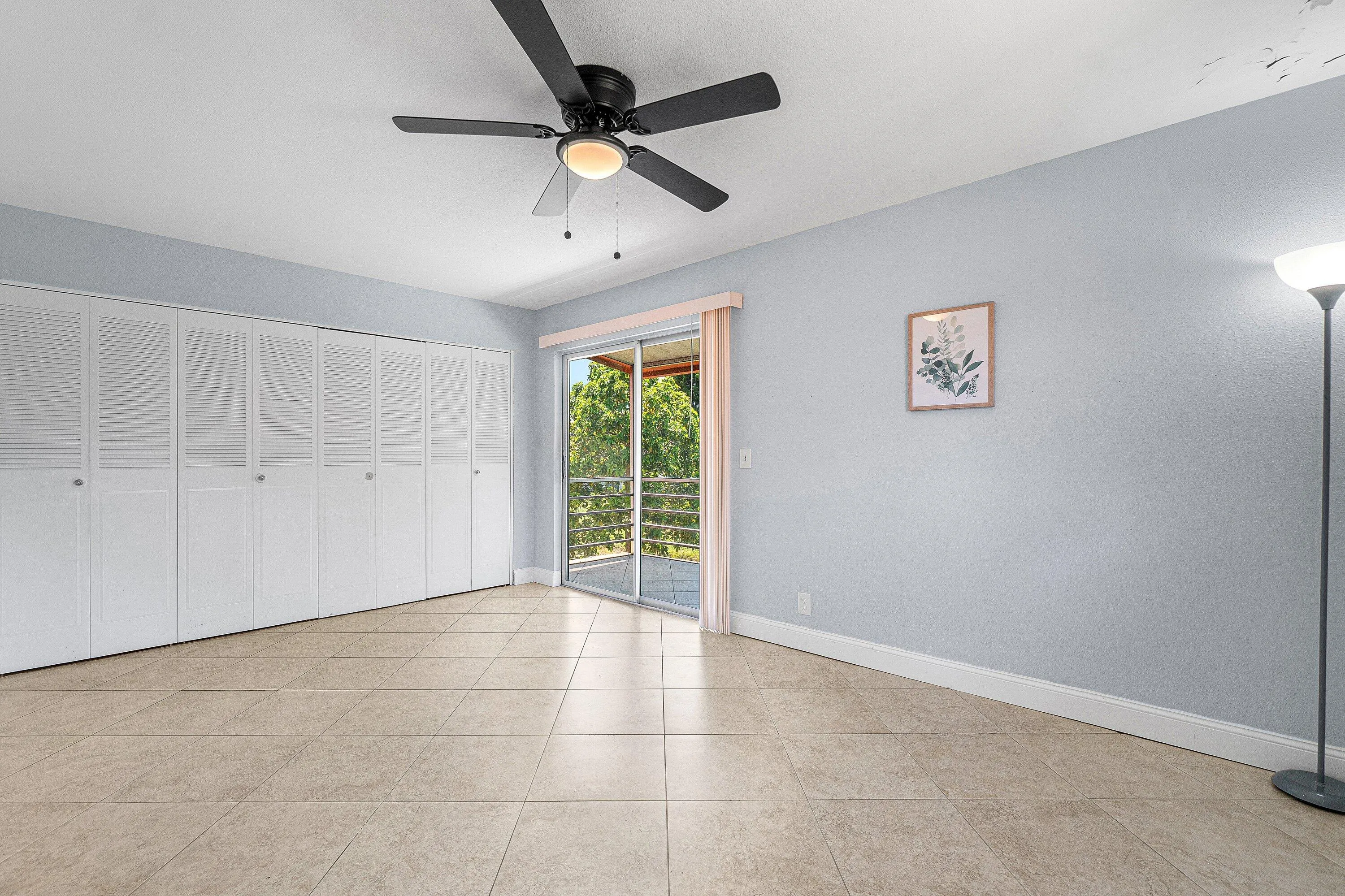 Expansive tile flooring, sliding glass door with balcony access, full-wall louvered closet doors, and ceiling fan with integrated lighting