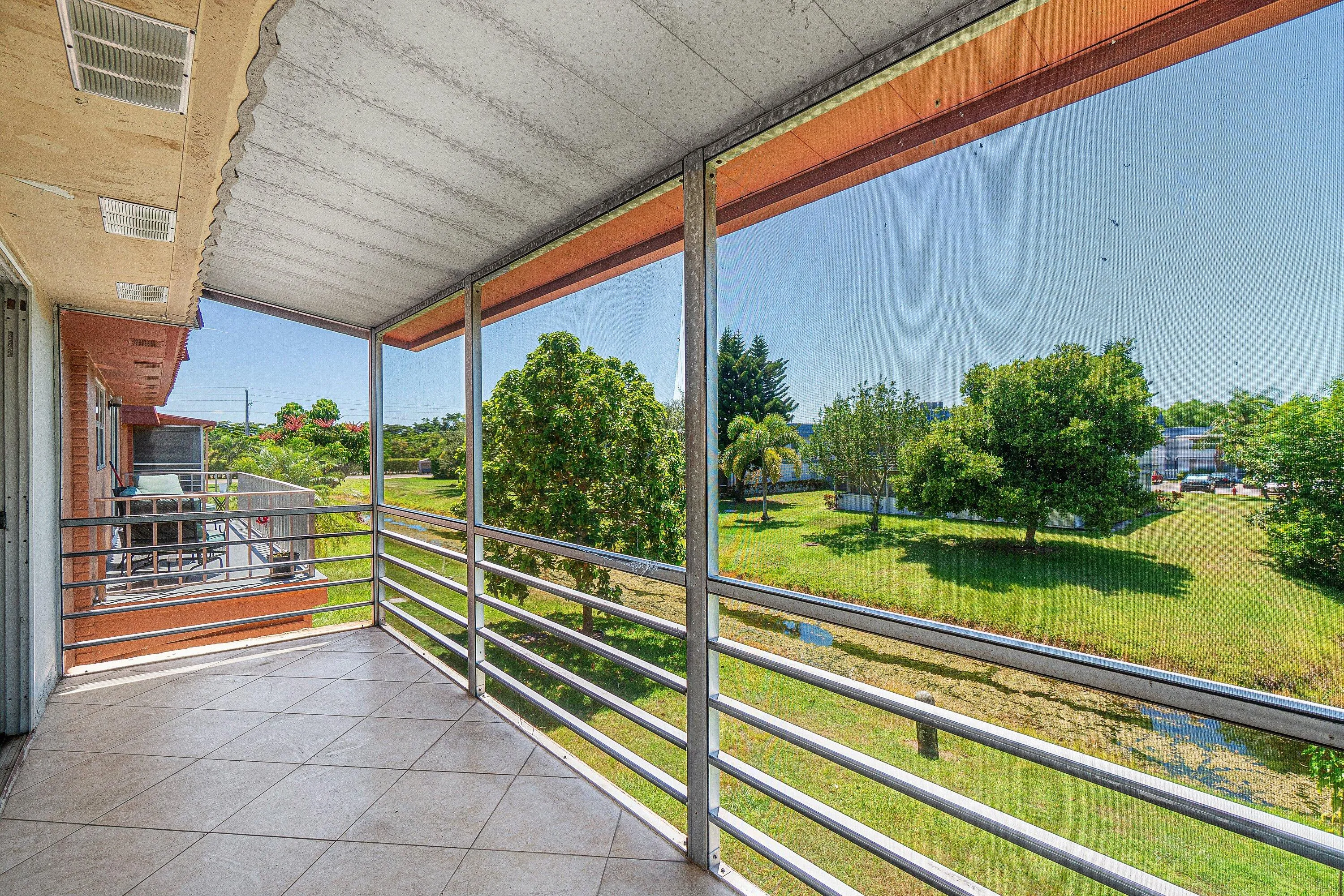 Screened balcony with tiled flooring and metal railing overlooking a landscaped green space with a water feature