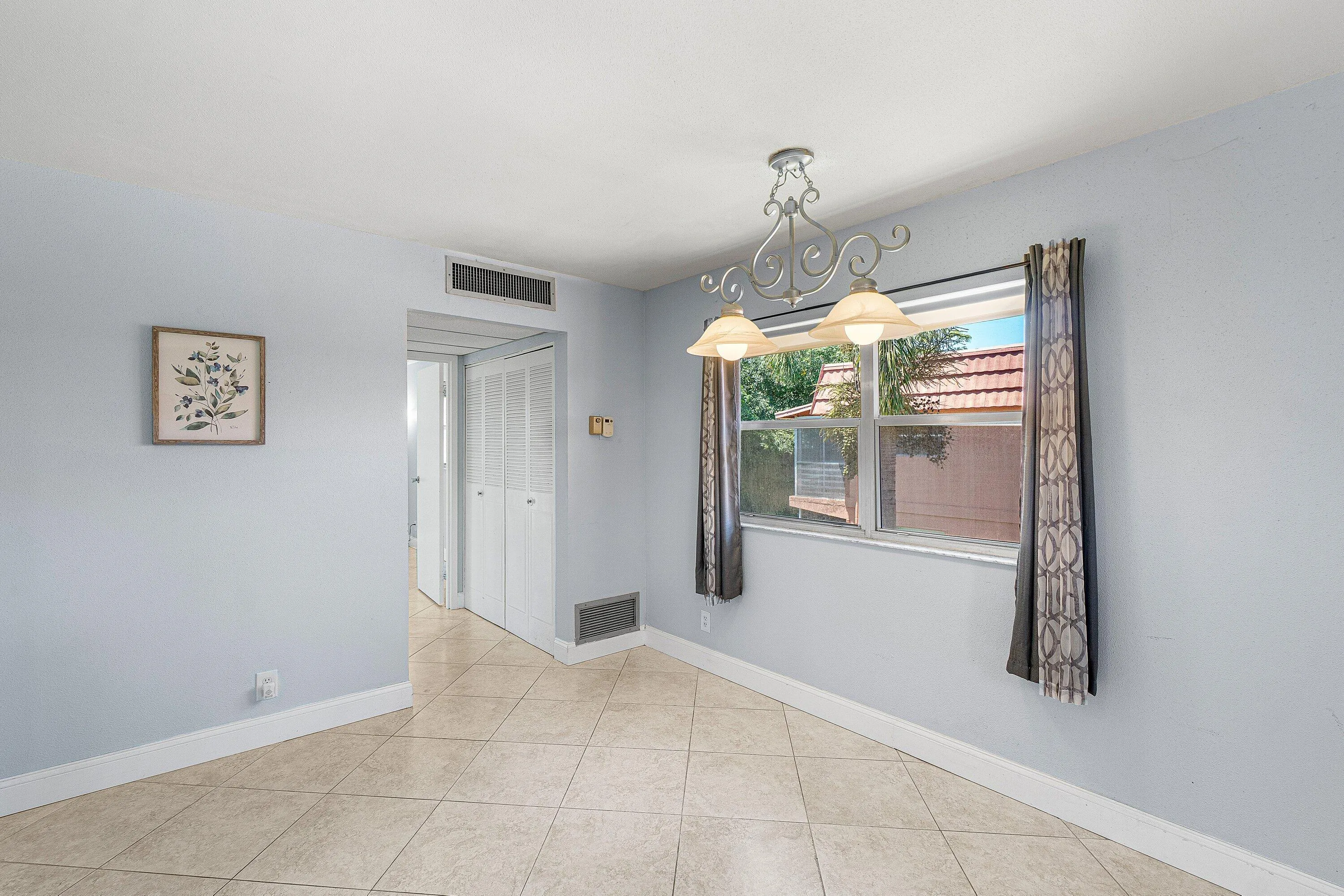 Tile flooring, wall-mounted air conditioning vent, and a window with exterior views