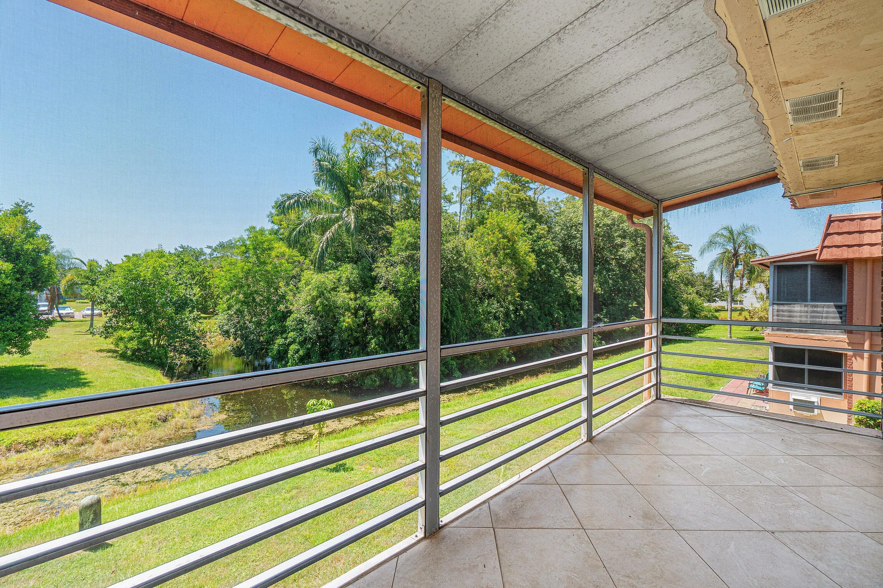 Screened balcony featuring tiled flooring and metal railings overlooking a water feature and tropical landscaping