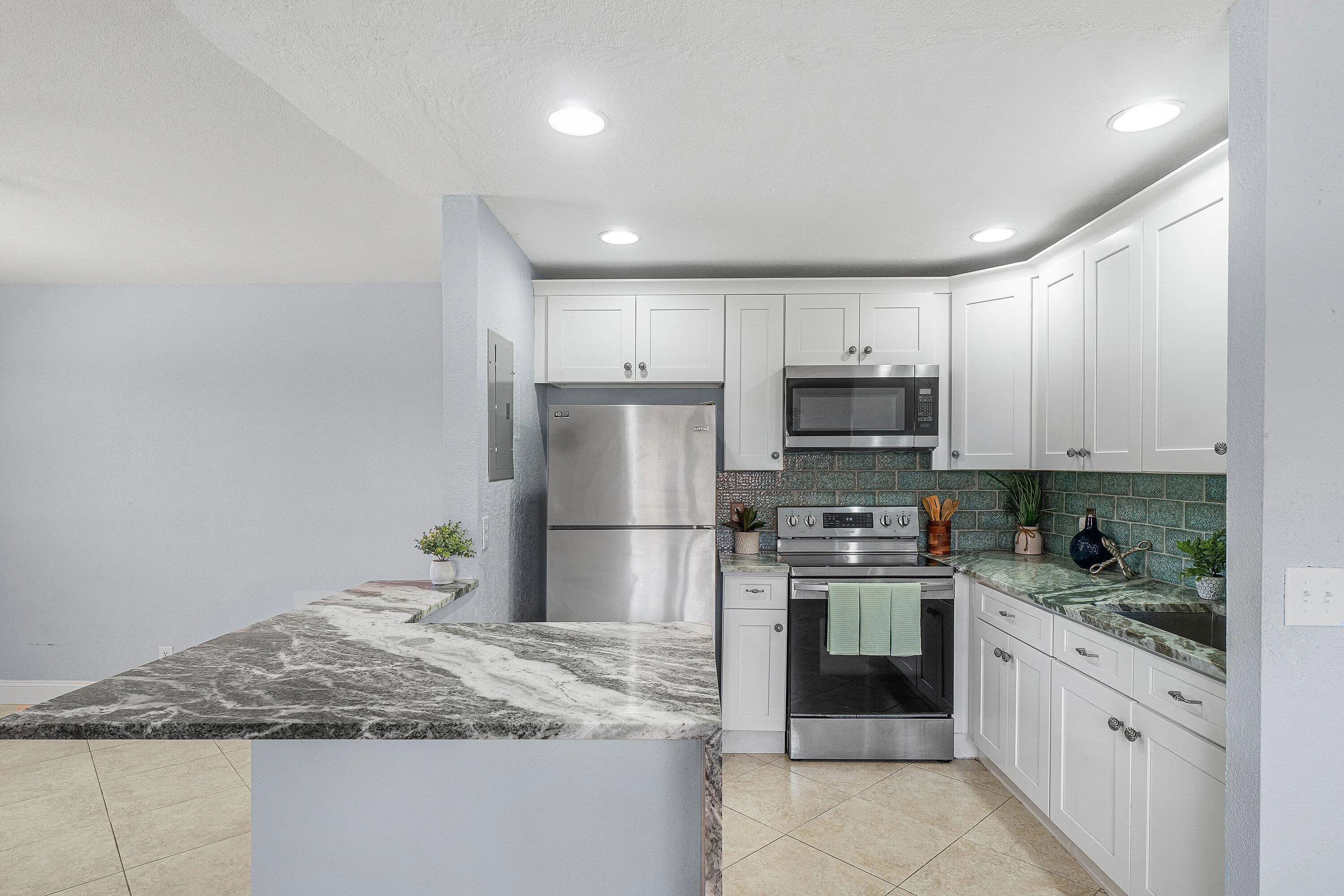 White shaker cabinetry, stainless steel appliances, patterned backsplash, recessed lighting, and patterned tile flooring