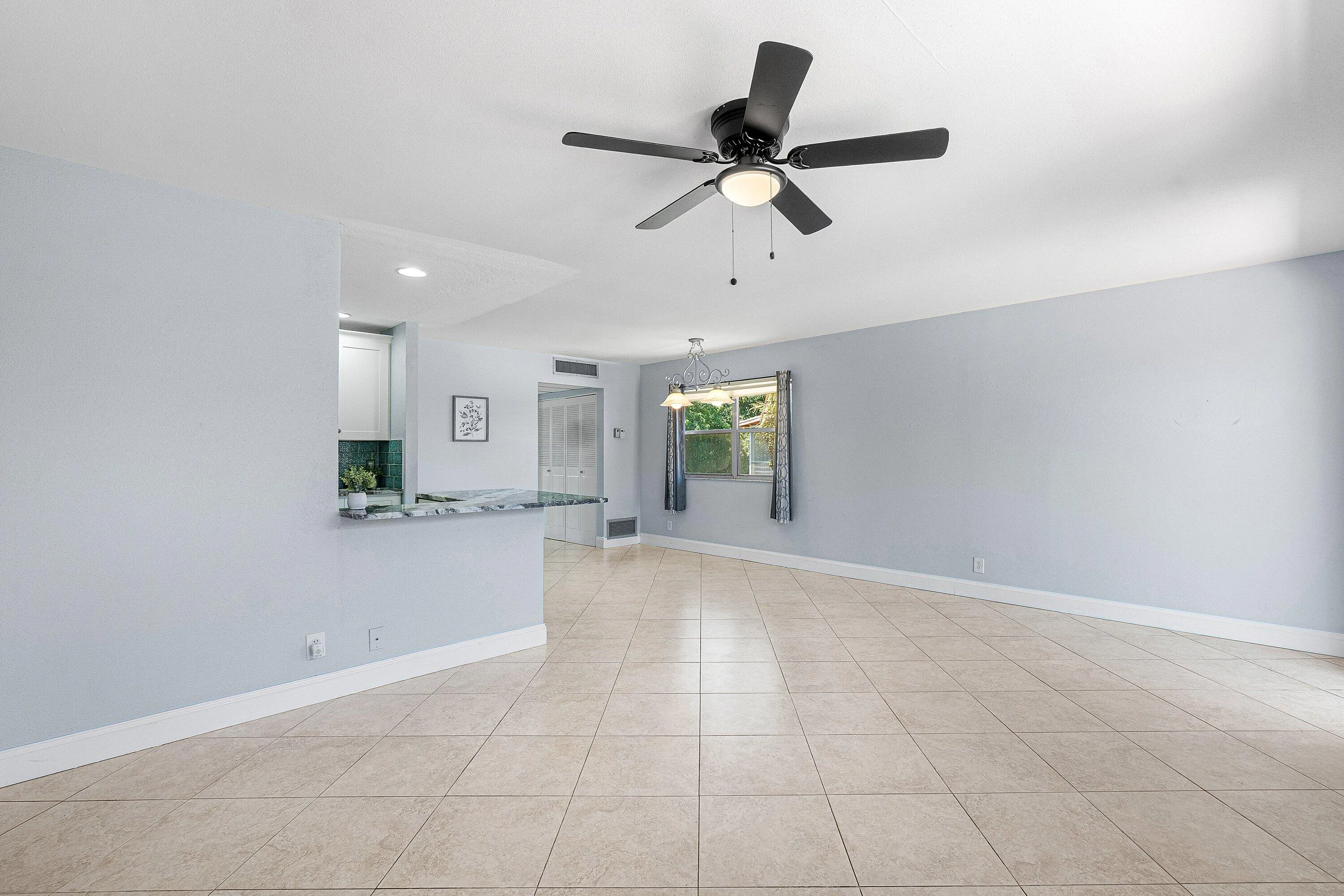 Tile flooring, ceiling fan with integrated lighting, window with drapes, and a half-wall with a counter surface