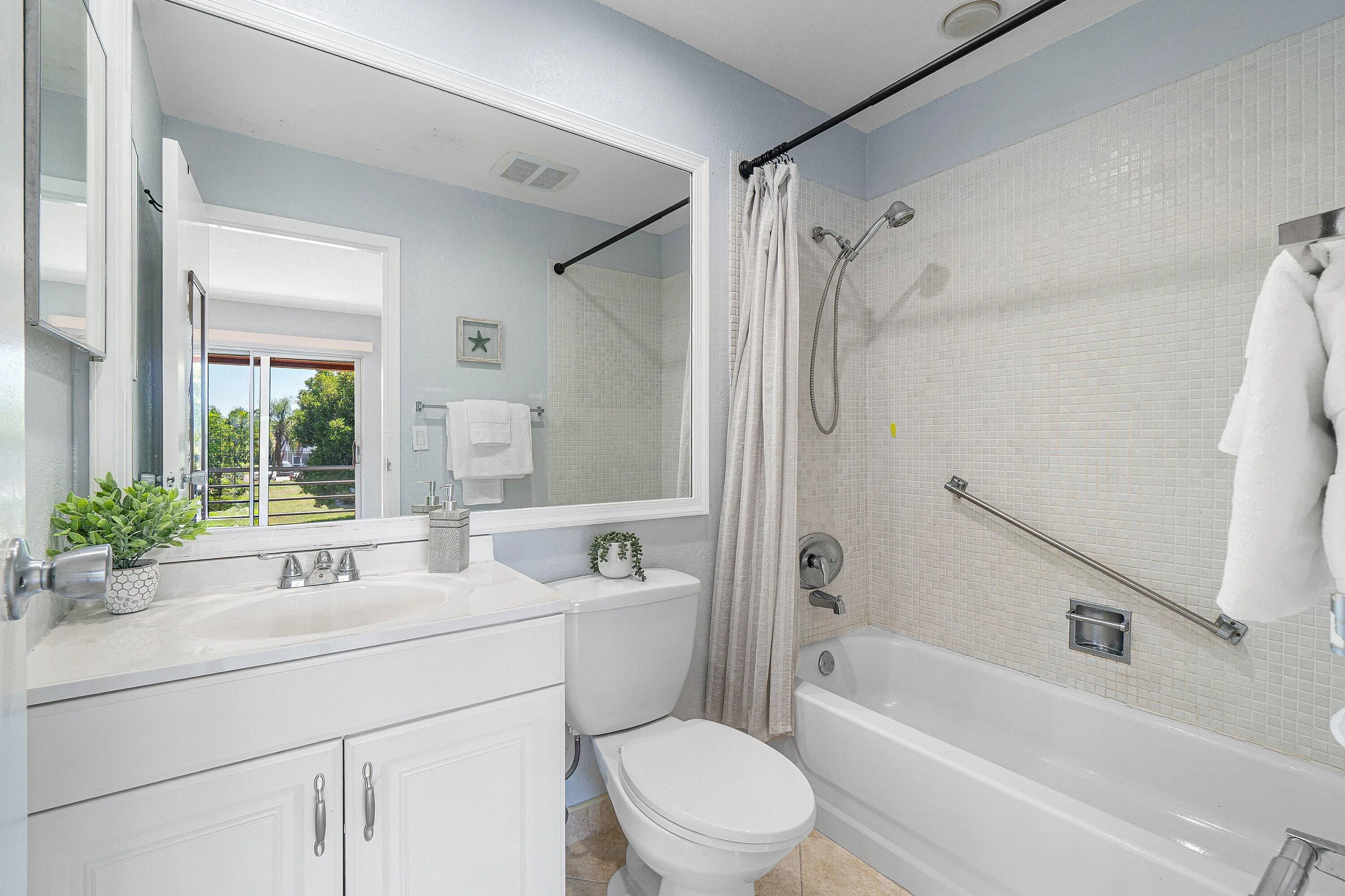 White vanity with an integrated sink and chrome faucet, white tiled tub surround, and a wall-mounted shower head