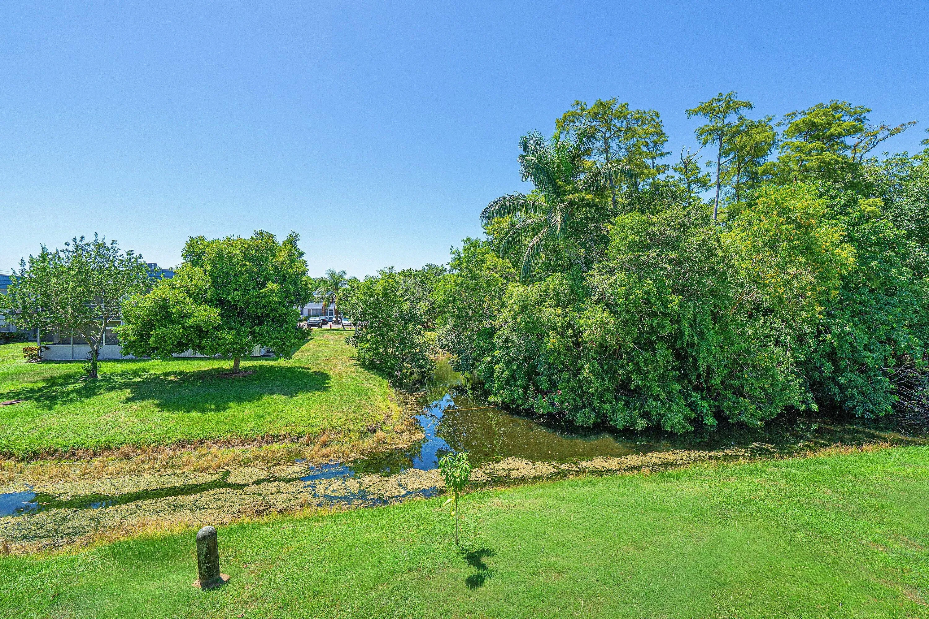 Expansive green space featuring a natural water element, mature trees, and lush landscaping