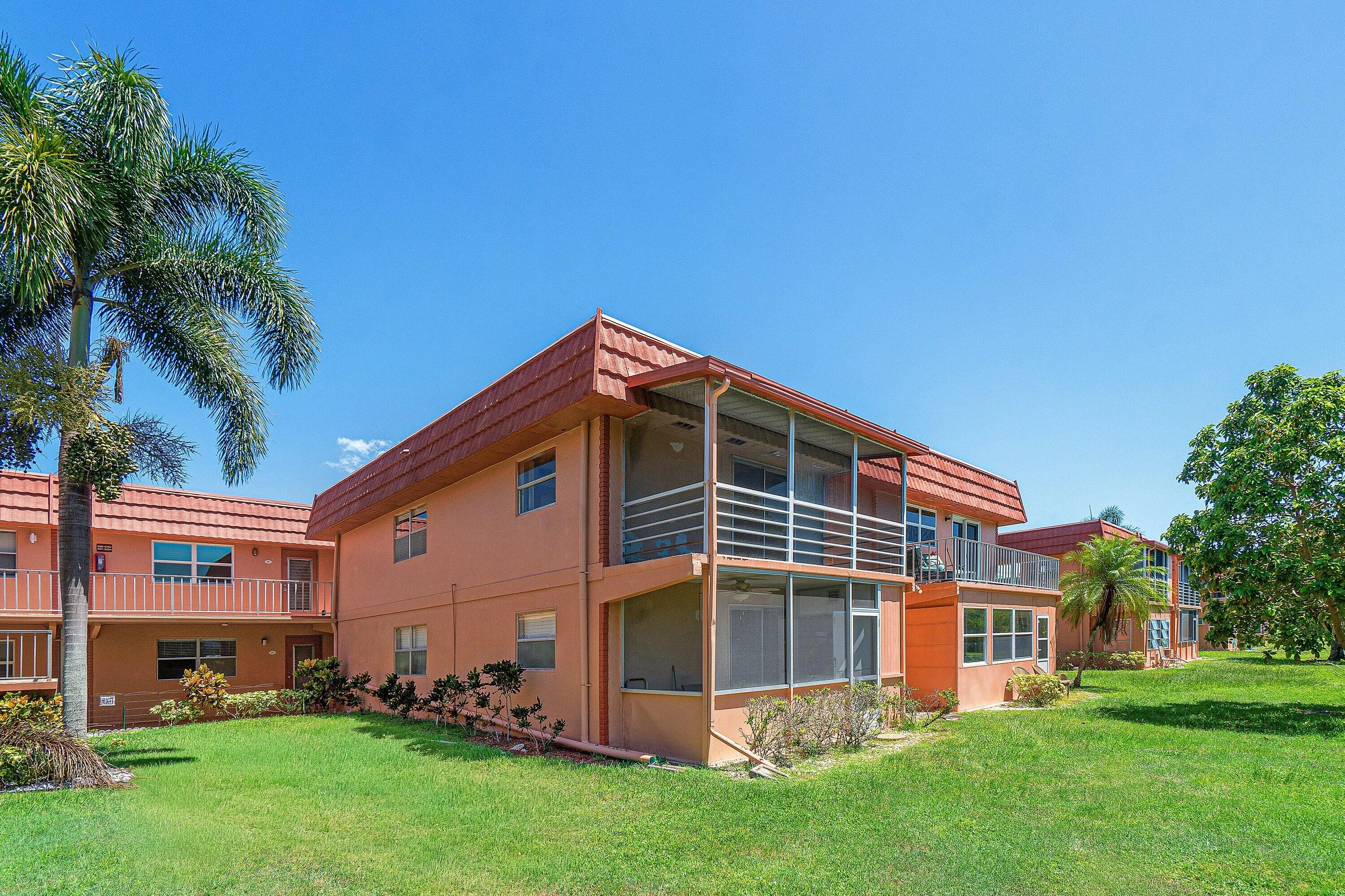 Exterior building with orange stucco finish, terracotta-style roof tiles, multiple screened balconies, and a manicured lawn