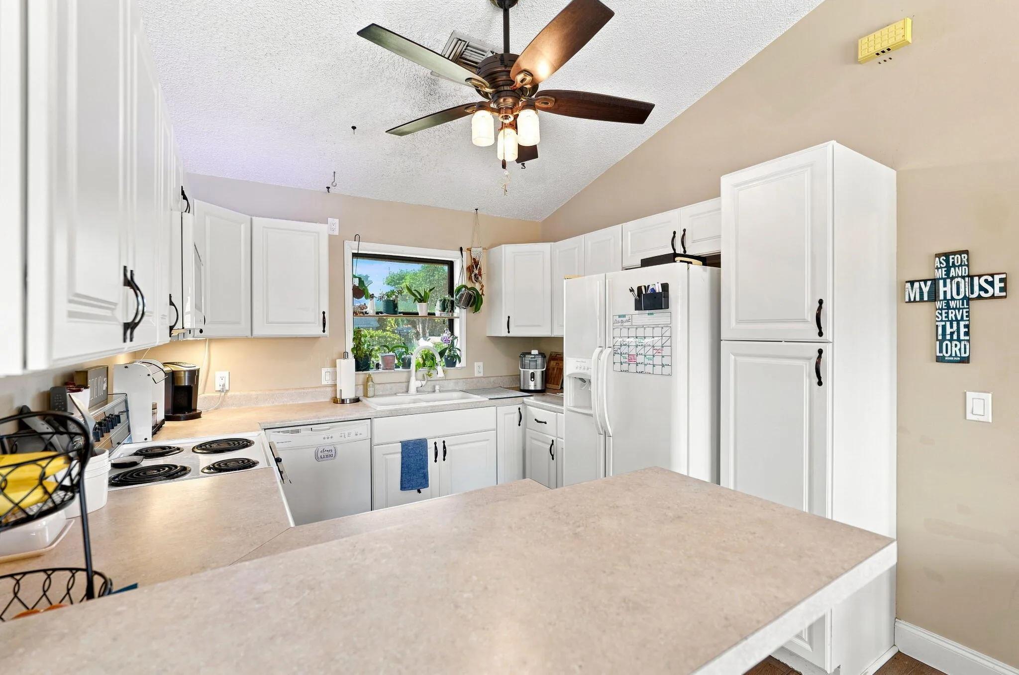 Vaulted ceiling with a ceiling fan, white cabinetry with black hardware, built-in dishwasher, and a window above the sink