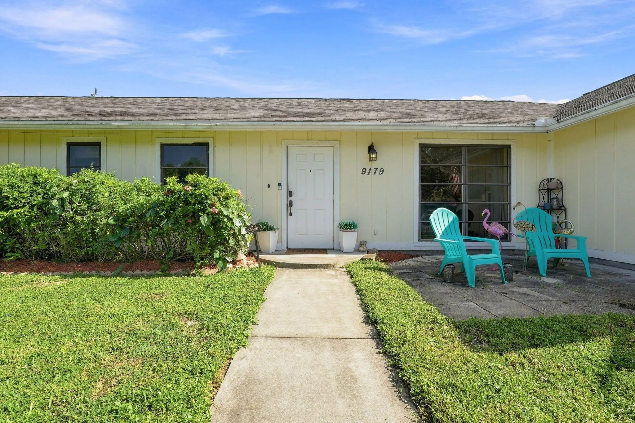 Single-story exterior with light-colored siding, a white front entry door, a paved walkway and a landscaped front yard with green lawn
