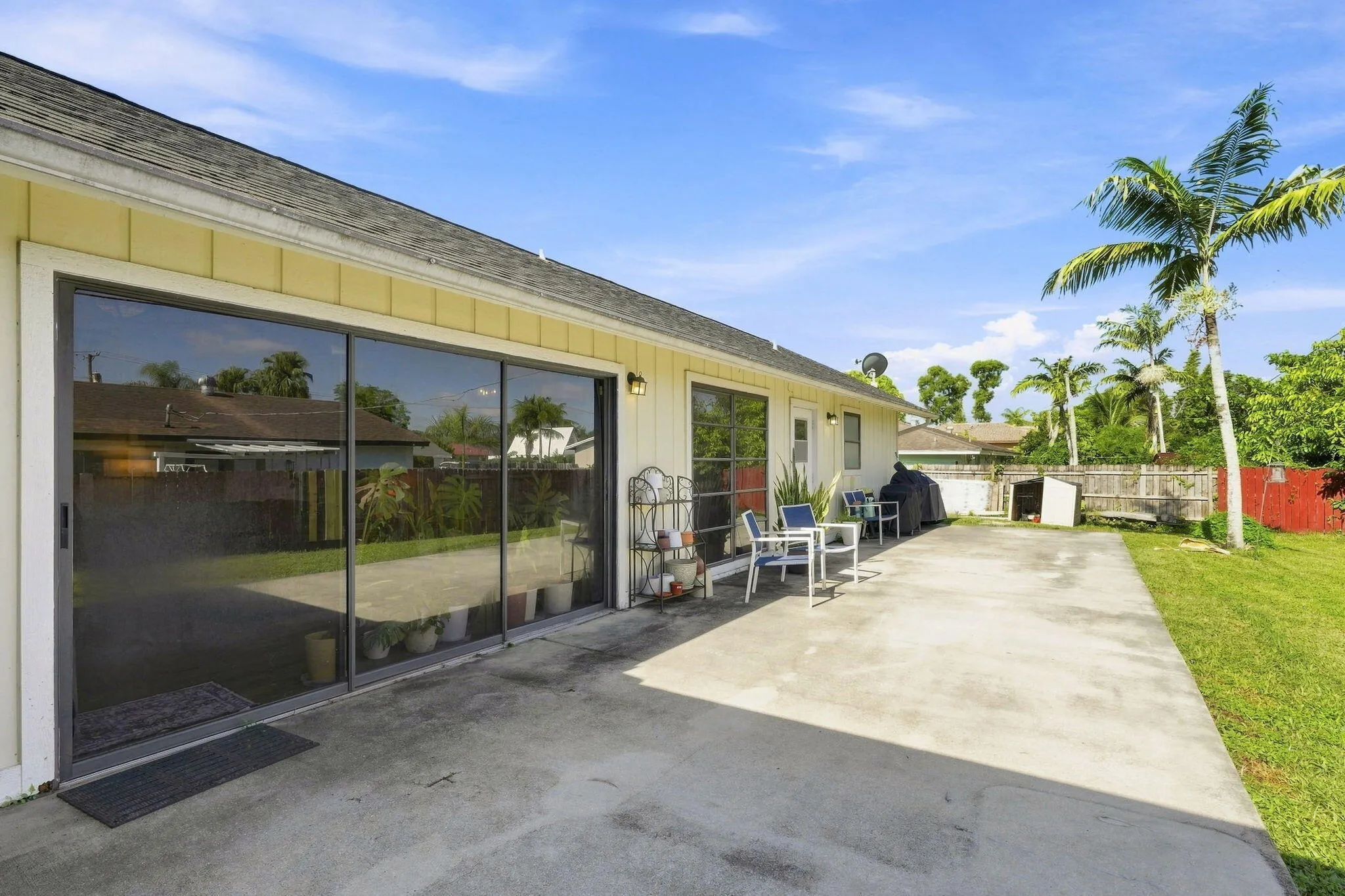 Expansive concrete patio, sliding glass doors, exterior lighting, green lawn and a mature palm tree
