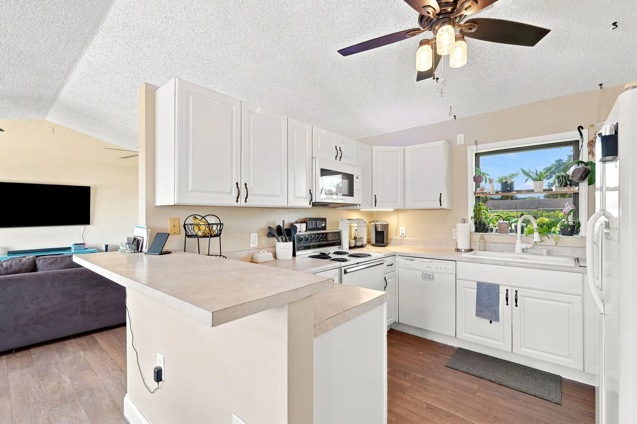 Kitchen featuring wood-finish flooring, white cabinetry, a composite countertop, and a window above the sink