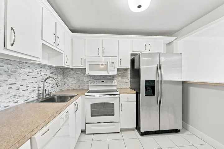 Kitchen featuring white cabinetry, stone-finish countertops, subway tile backsplash, stainless steel refrigerator, and white tile flooring