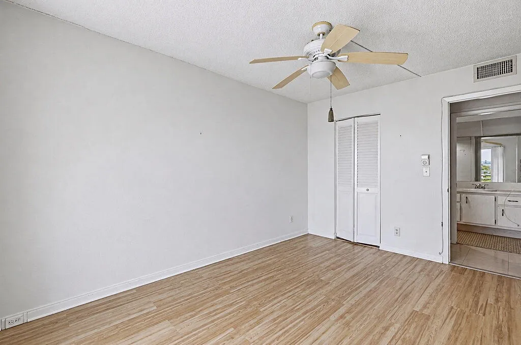 Wood-finish flooring, ceiling fan with light, bi-fold louvered closet doors, and an open doorway to a bathroom with a vanity