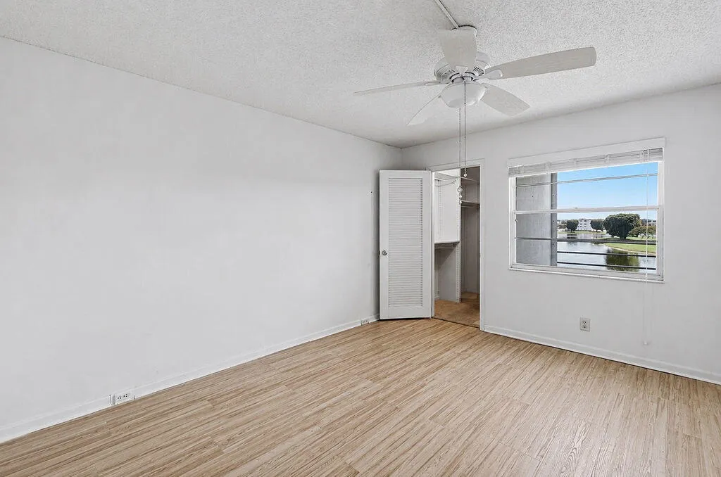 Wood-finish flooring, ceiling fan, louvered bi-fold closet door, and a window with a water feature backdrop