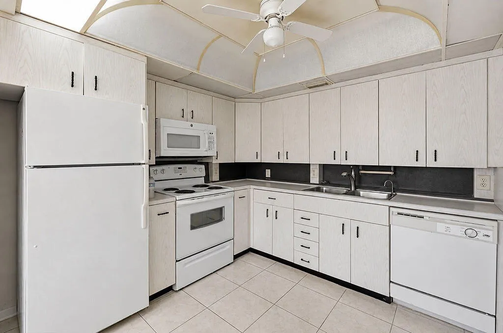Kitchen featuring white appliances, upper and lower cabinetry, a double basin sink, and tile flooring